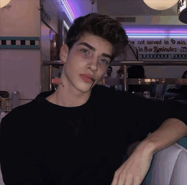 a young man with a cigarette in his mouth is sitting at a table in a diner .