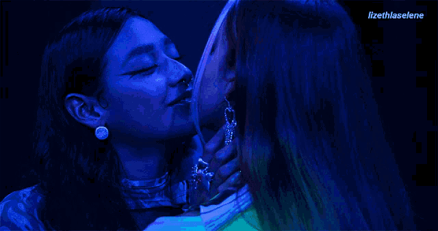 two women are kissing each other in a dark room with a blue light behind them .