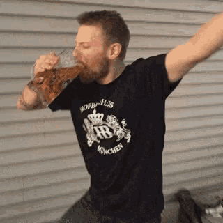 a man wearing a black shirt that says hb munchen is drinking from a glass