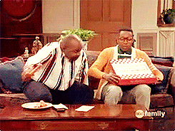 two men are sitting on a couch and one is holding a pizza box that says family on it