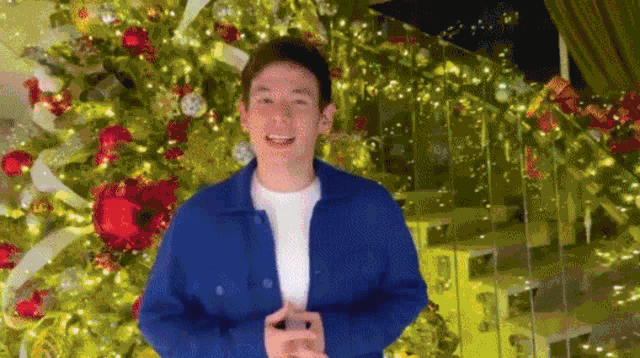 a young man is standing in front of a christmas tree .