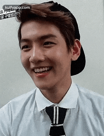 a young man wearing a hat and tie is smiling and looking at the camera .