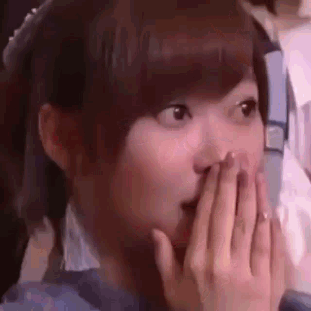 a woman is covering her mouth with her hands and looking surprised .