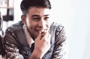 a man in a denim jacket is smiling with his hand on his chin .