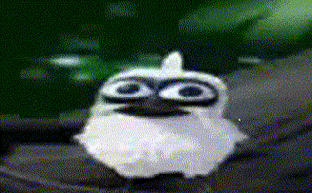 a white owl with black eyes is sitting on a green surface