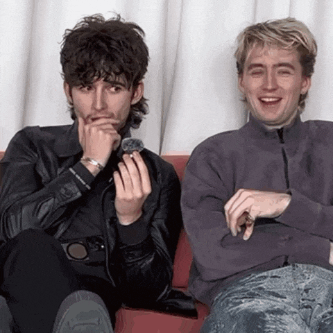 two men are sitting next to each other on a couch and one is holding a ring in his hand .