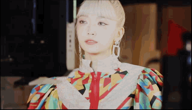 a woman wearing a colorful jacket and earrings looks at the camera