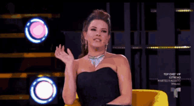 a woman in a black dress is sitting in a yellow chair on top chef vip