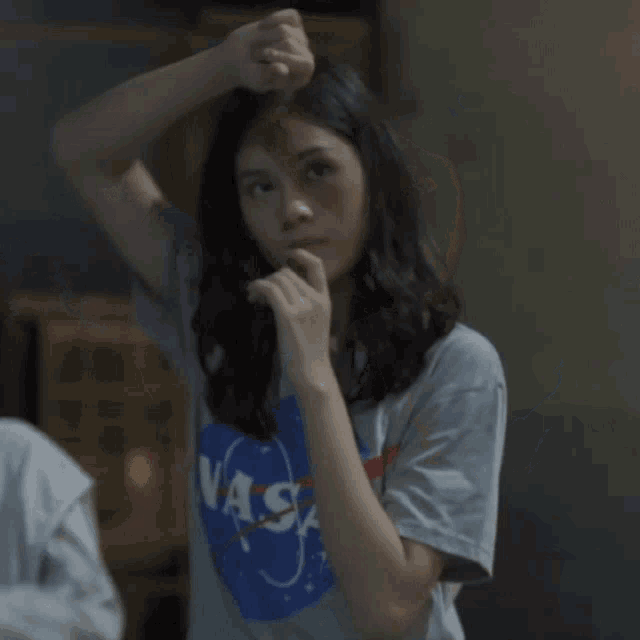 a woman wearing a nasa shirt holds her finger to her chin