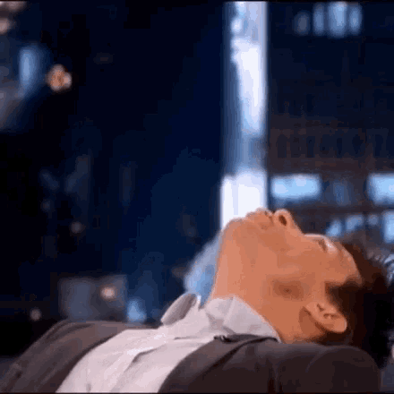 a man in a suit and white shirt is laying on a couch with his head down .