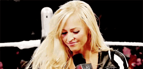 a blonde woman is sitting in a wrestling ring with a microphone in her hand .