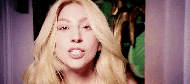 a close up of a woman 's face with blonde hair and a green background .