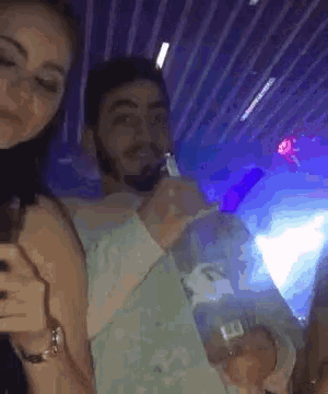 a man with a beard is drinking from a bottle while a woman looks on