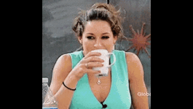 a woman in a blue tank top is drinking from a white mug .