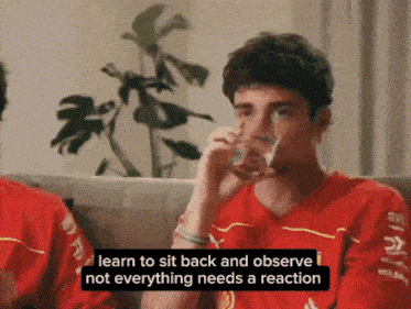 a man in a red shirt is sitting on a couch drinking a glass of water and saying " learn to sit back and observe "