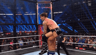 a wrestler is being lifted by another wrestler in a wrestling ring with a crowd watching