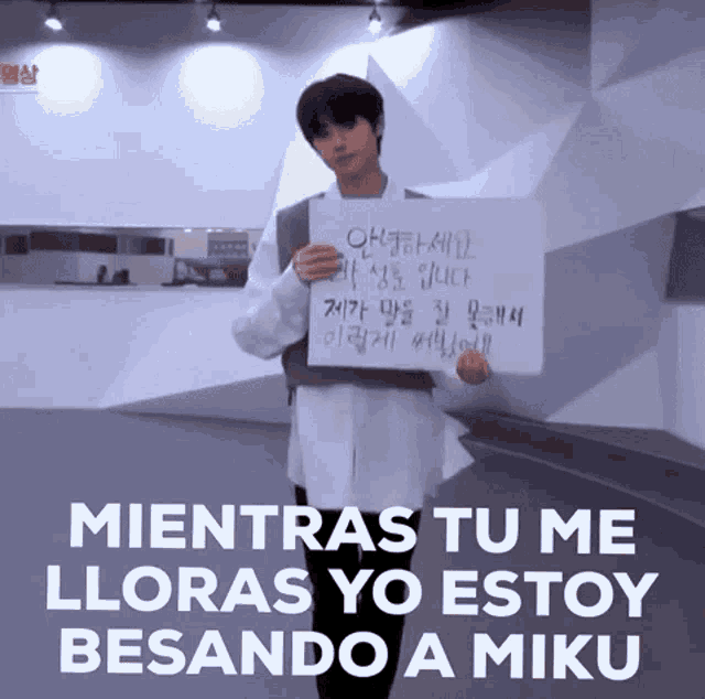 a young man holding a sign that says mientras tu me lloras yo estoy besando a miku