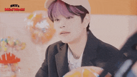 a young man with purple hair and a hat is sitting at a table with a bowl of candy .