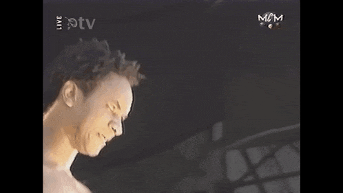 a man without a shirt is playing a guitar in front of a tv screen .