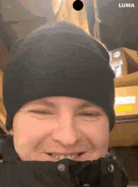a man wearing a black beanie and a black jacket is smiling with a luma logo in the upper right corner