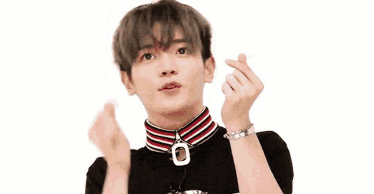 a young man is making a heart shape with his hands while wearing a choker and a necklace .