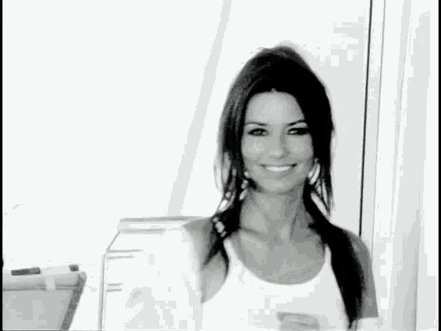 a black and white photo of a smiling woman in a white tank top .