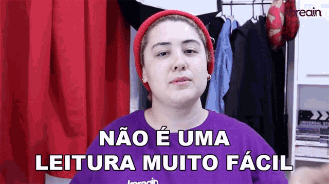 a woman wearing a purple shirt and a red hat says " não e uma leitura muito facil "