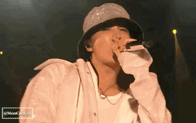 a man wearing a hat is singing into a microphone on stage .