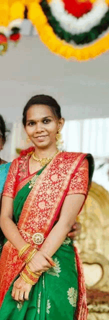 a woman wearing a green and red saree is smiling