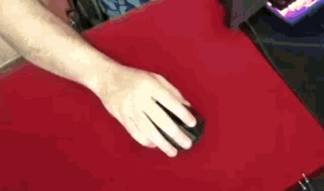 a close up of a person 's hand pressing a mouse on a red surface