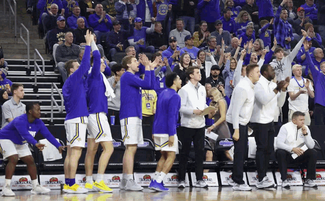 a group of basketball players are standing on a court in front of a crowd that is wearing blue and yellow shirts with the number 24