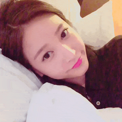 a close up of a woman laying on a bed with a button on her shirt