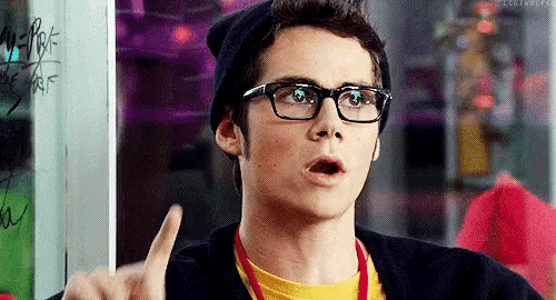 a young man wearing glasses and a beanie is pointing up at something