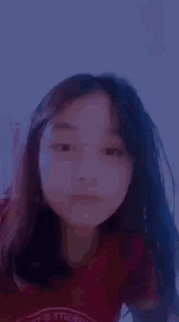 a young girl with long black hair is making a funny face while wearing a red shirt .