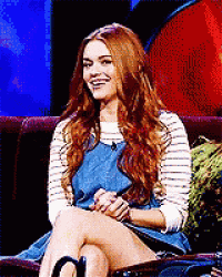 a woman with long red hair is sitting on a couch with her legs crossed .