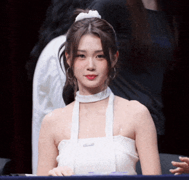 a woman wearing a white halter top with a clear strap around her neck looks at the camera