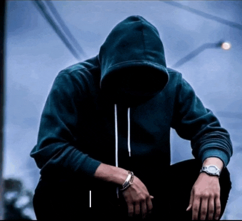 a man wearing a hoodie and a watch sits with his hands on his knees