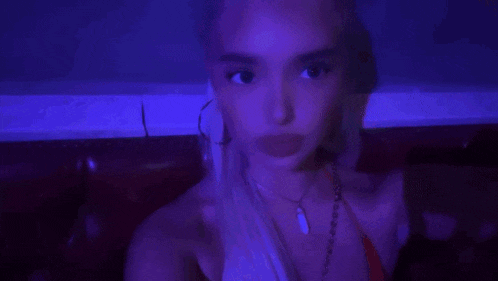 a woman in a red bikini is sitting on a red couch in a dark room with purple lights behind her .