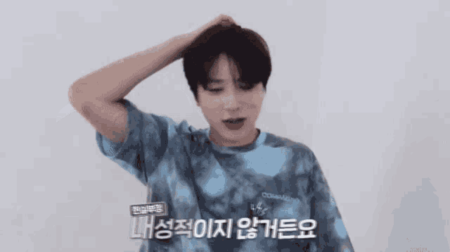 a young man wearing a blue tie dye shirt holds his head