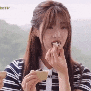 a woman in a striped shirt is eating a piece of bread .