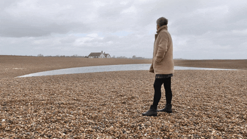 a woman standing on a beach looking at a house