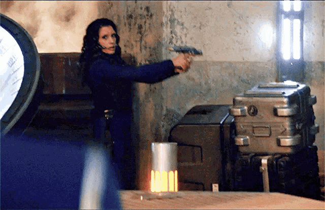 a woman is holding a gun in a room with a suitcase