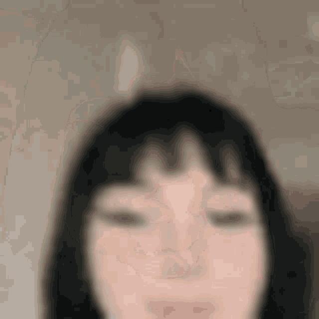 a blurry picture of a woman 's face with short black hair and bangs .