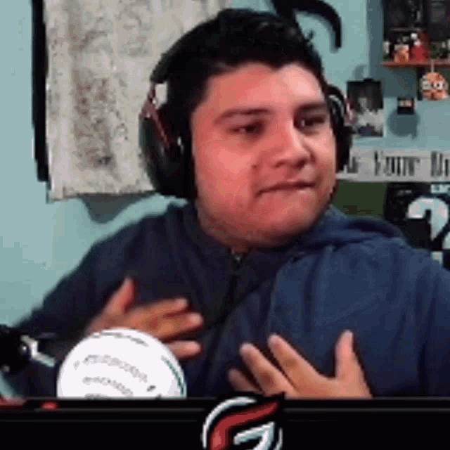 a man wearing headphones holds his hands to his chest while sitting in front of a microphone