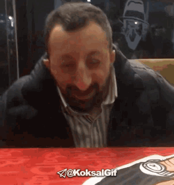 a man with a beard is sitting at a table with the hashtag @koksalgif on the bottom