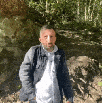 a man with a beard and a nose mask is standing in a forest .