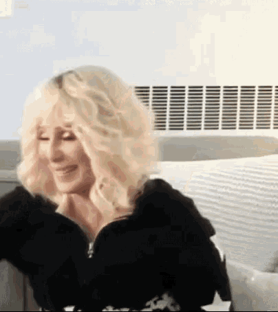 a woman with blonde hair is sitting on a couch in front of an air conditioner .