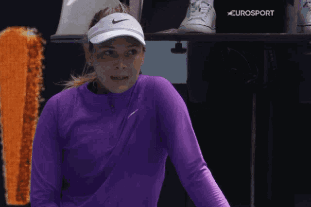 a woman wearing a purple shirt and a white nike visor is standing in front of a eurosport sign