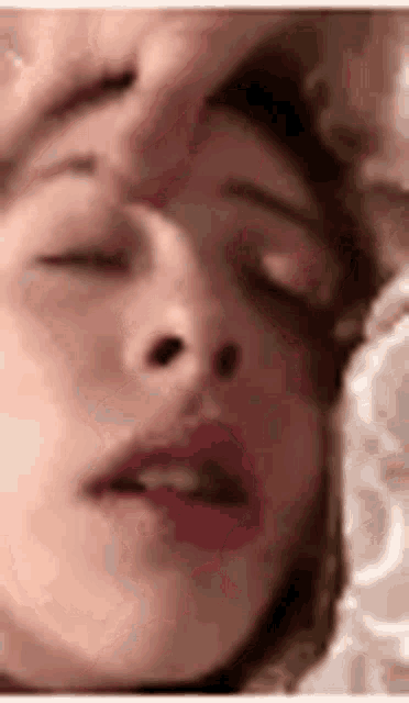 a woman is sleeping with her eyes closed and a man is touching her face .