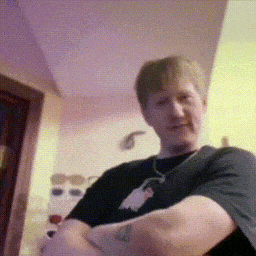 a man with a tattoo on his arm is sitting in a room with his arms crossed .